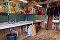 Rustikale Werkstatt in Hitra, Norwegen: Angelzubehör, bunte Rettungswesten und Seile an Holzwänden. Edelstahlspüle, Arbeitsflächen und robuste Ausstattung schaffen eine praktische Umgebung für Angler. Perfekt für Vorbereitungen und Ausrüstungspflege vor dem Meeresangeln.