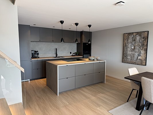 Moderne Küche in Südwest-Norwegen: Graue Einbauschränke, Insel mit Arbeitsfläche, Holzfußboden, Hängelampen und stilvolle Dekoration sorgen für skandinavisches Ambiente und zeitloses Design. Ideal für komfortables Wohnen und entspannten Angelurlaub.