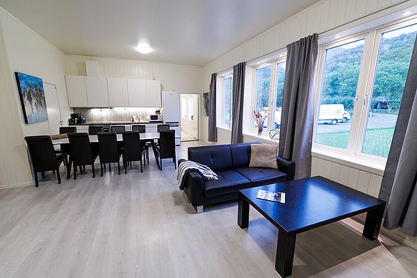 Einladende Ferienwohnung in Nordland, Norwegen: Moderne Küche, geräumiger Wohnbereich mit gemütlicher Couch, großer Esstisch und helle Fenster bieten Komfort nach einem erfolgreichen Angeltag. Ideal für Angelreisen und Naturerlebnisse.