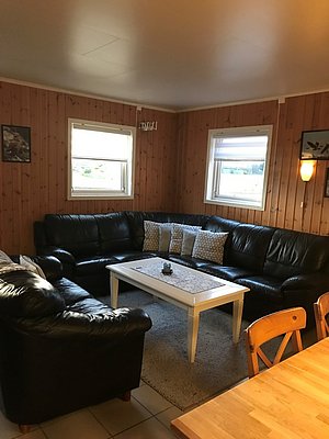 Gemütliches Wohnzimmer mit Holzwänden in einer Ferienhütte in Hitra, Norwegen. Schwarze Ledersofas und ein weißer Couchtisch bieten Entspannung nach einem erfolgreichen Angeltag. Ideal für Angelurlauber und Ruhesuchende.