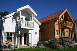 Gemütliche Ferienhäuser in Süd-Norwegen unter strahlend blauem Himmel. Traditionelle, helle Holzarchitektur mit roten Dächern, umgeben von Felsen und grüner Natur. Perfekt für Angelreisen und Erholung in malerischer Umgebung.