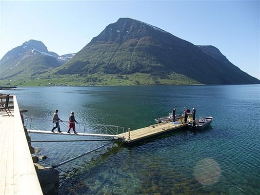 Klarer Fjord in Nordland, Norwegen: Steg mit Anglern vor beeindruckender Bergkulisse bei Sonnenschein. Ideal für Angelurlaub und Naturerlebnis. Perfekte Kombination aus Abenteuer und Entspannung in traumhafter Landschaft.