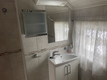 Helles Badezimmer in Nord-Norwegen mit weißem Waschbecken, elegantem Spiegel, gefliesten Wänden, Duschvorhang und natürlichem Licht durch ein Fenster. Ideal für komfortable Erholung nach Abenteuern beim Angelurlaub.