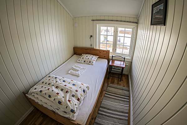 Gemütliches, helles Einzelzimmer in Nordnorwegen mit Holzwänden, Einzelbett, kleinem Tisch und Blick aus dem Fenster. Ideal für Reisende, die Naturerlebnisse und Angelabenteuer in Norwegen genießen möchten.