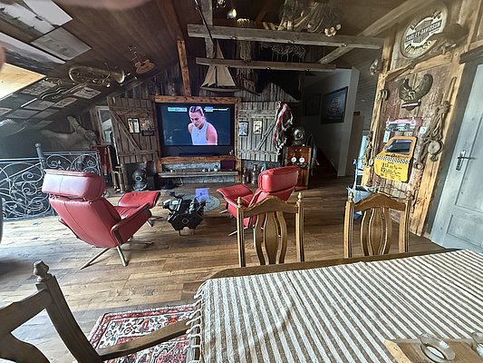 Gemütliches nordisches Wohnzimmer in Nord-Norwegen, mit roten Sesseln, Holzwänden und einem großen Fernseher. Rustikale Einrichtung, ideal zum Entspannen nach einem Tag beim Angeln. Perfekte Kombination aus traditionellem Charme und modernem Komfort.