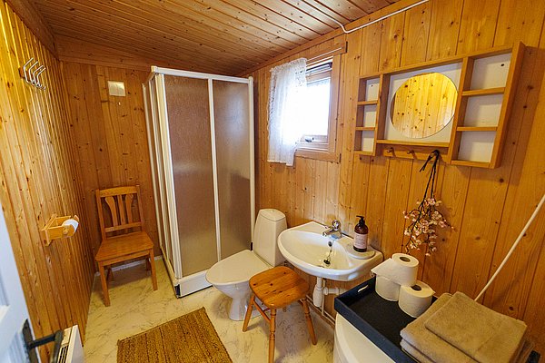 Gemütliches, skandinavisches Badezimmer mit Holzvertäfelung in Hitra, Norwegen. Ausgestattet mit Dusche, Toilette, Waschbecken und Spiegel. Ideal für Angelsportler, die Komfort und Tradition suchen. Warmes, einladendes Ambiente für den perfekten Angelurlaub.