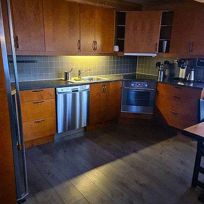 Gemütliche Holzküche in Nord-Norwegen mit modernen Geräten, Waschbecken, Backofen und Geschirrspüler. Warme Holzverkleidungen kombiniert mit grauen Fliesen schaffen eine einladende Atmosphäre. Ideal für Angler auf Erholungsreise.