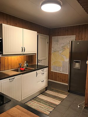 Gemütliche Küche in einer Hütte in Hitra, Norwegen. Holzverkleidung, moderne Ausstattung, heller Teppich und Wandkarte. Ideal für Angelurlauber, die Komfort und Funktionalität suchen. Perfekt für gesellige Abende nach erfolgreichen Angeltouren.