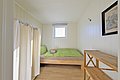 Ein schlichtes, gemütliches Schlafraum in Nordland, Norwegen, mit Holzbett, grünem Bettzeug, einem Fenster, Vorhang und Regal. Ideal für Ruhe und Entspannung nach einem aufregenden Angelurlaub in faszinierender Natur.