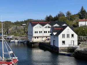 Ein idyllischer Hafen in Südwest-Norwegen zeigt weiße, traditionelle Gebäude direkt am Wasser, umgeben von üppiger Natur. Perfekt für Angler und Naturliebhaber, die Norwegens atemberaubende Landschaft erleben möchten.