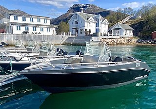 Ein beeindruckender Hafen in Nordland, Norwegen: Moderne Aluminiumboote vor malerischer Bergkulisse und stilvollen Holzhäusern bieten ideale Bedingungen für unvergessliche Angelreisen und Küstenerkundungen. Perfekter Angelurlaub in skandinavischer Natur.