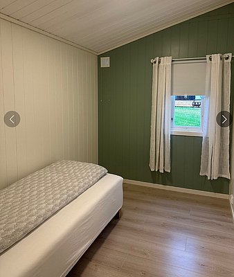 Gemütliches Schlafzimmer in Hitra, Norwegen: Einzelbett, grüne Wand, kleine Fensteransicht mit Vorhängen. Ruhig und einladend, ideal für Angelurlauber. Entspanne hier nach einem aufregenden Tag voller Abenteuer und Fänge.