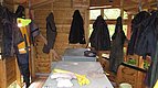Holzhütte in Hitra, Norwegen, mit hängenden Regenjacken und Arbeitskleidung. Auf dem Tisch liegen Handschuhe und Ausrüstung. Perfekt für Angler, die Schutz und Komfort suchen. Abenteuerliches Angelreiseziel in natürlicher Umgebung.