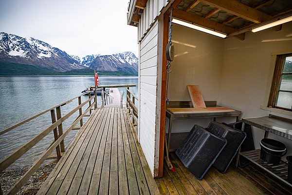 Eine Angelhütte in Nord-Norwegen mit Holzsteg, umgeben von schneebedeckten Bergen und einem ruhigen Fjord. Ideal für Angelreisen und Naturerlebnisse in skandinavischer Landschaft.