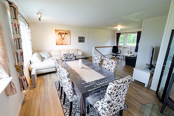 Helles Wohnzimmer in Nord-Norwegen mit gemütlicher Sofaecke, großem Esstisch und modernem Fernseher. Geschmackvolle Dekoration und lichtdurchflutete Fenster schaffen eine einladende Atmosphäre für entspannte Angelreisen.