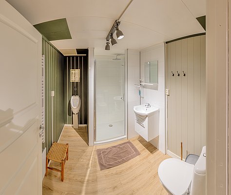Modernes Badezimmer in Nordland, Norwegen, mit Dusche, WC, Urinal und Waschbecken. Holzoptik-Boden sorgt für gemütliches Ambiente. Ideal für Angelurlaub-Unterkünfte in skandinavischem Stil. Barrierefreie Einrichtung für Komfort nach einem Tag am Wasser.