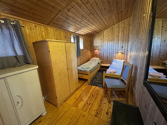 Gemütliches Zimmer in Hitra, Norwegen, mit Holzwänden, zwei Einzelbetten und einfacher Möblierung. Ideal für Angler, die nach einem erfolgreichen Tag in den norwegischen Gewässern eine erholsame Ruhepause suchen.