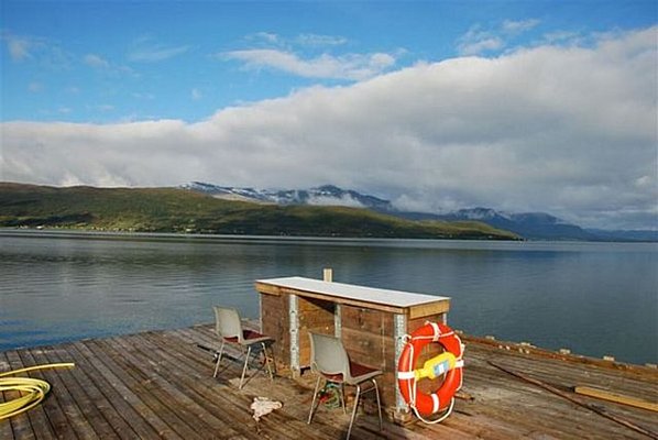 Holzsteg in Nord-Norwegen mit Blick auf fjordartige Landschaft und schneebedeckte Berge bei bewölktem Himmel. Perfekter Ort für Angelurlaub in Norwegen.