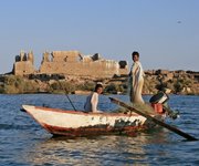 Zwei Männer in einem Fischereiboot fahren auf einem Fluss in der Nähe antiker Ruinen.