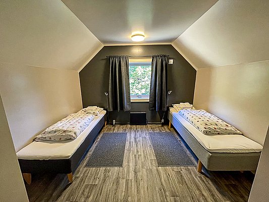 Gemütliches Schlafzimmer in Nord-Norwegen mit zwei Einzelbetten, Holzfußboden und natürlichem Licht. Perfekt für Angelreisen und Entspannung in der nordischen Natur. Skandinavisches Design, ideal für Erholung nach einem Tag am Wasser.