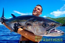 Ein Angler hält stolz einen großen Wahoo im klaren Wasser vor Tansanias Küste. Perfekte Bedingungen für ein unvergessliches Meeresangelabenteuer. Vitória!