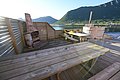 Holzterrasse mit Grill und Hot Tub in Nord-Norwegen, Blick auf malerischen Fjord und Berge, ideal für entspannte Angelurlaub-Momente. Perfekte Kulisse für Outdoor-Abenteuer und Erholung inmitten atemberaubender Natur.
