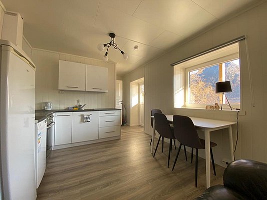 Gemütliche, moderne Wohnküche in Nord-Norwegen mit hellen Holzfußböden, großzügigem Fensterblick auf herbstliche Landschaft, weißer Küchenzeile und Esstisch für zwei Personen. Perfekt für Angelurlaube in ruhiger, naturnaher Umgebung.
