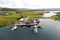 Nordland, Norwegen: Rote Hütten und Boote an einem charmanten Fjordufer, umgeben von grüner Landschaft. Perfekter Ausgangspunkt für Angelreisen und Naturliebhaber. Atemberaubende Kulisse für unvergessliche Abenteuer im skandinavischen Stil.