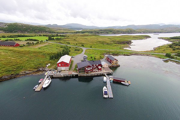 Nordland, Norwegen: Rote Hütten und Boote an einem charmanten Fjordufer, umgeben von grüner Landschaft. Perfekter Ausgangspunkt für Angelreisen und Naturliebhaber. Atemberaubende Kulisse für unvergessliche Abenteuer im skandinavischen Stil.