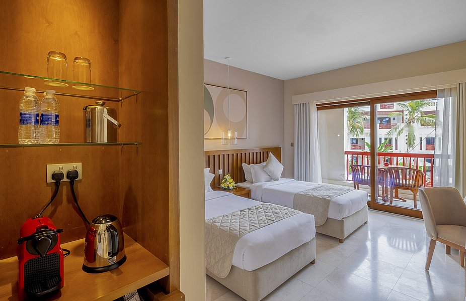 Helles Hotelzimmer in Süd-Norwegen mit zwei Einzelbetten, Balkon und Sitzecke. Eine Nespresso-Maschine und Wasserkocher stehen im Regal bereit. Ideal für erholsame Angelurlaube in der malerischen norwegischen Natur.