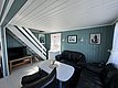 Gemütliches Wohnzimmer in Hitra, Norwegen: Moderne Einrichtung mit schwarzen Ledersofas, Holztisch und Treppe. Helle Wände mit Fischbildern schaffen maritimes Flair. Ideal für entspannenden Angelurlaub.