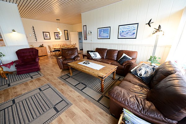 Gemütliches Wohnzimmer in Nord-Norwegen mit Ledersofas, Holztisch und dekorativen Kissen. Helle Holzwände und Kunstwerke schaffen eine einladende Atmosphäre. Perfekt für entspannte Abende nach einem erfolgreichen Angeltag in der malerischen Region.