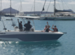 Ein Motorboot in der Bucht von São Vicente, Kapverden, mit fröhlichen Anglern. Im Hintergrund liegt der Hafen mit mehreren Segelbooten vor der beeindruckenden Berglandschaft. Perfekt für Angelreisen und Meeresabenteuer.