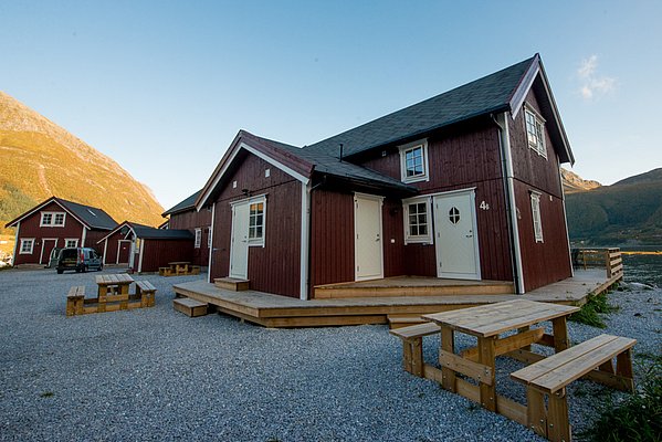 Eine idyllische, rot gestrichene Hütte in Nordland, Norwegen, umgeben von majestätischen Bergen und einem klaren See, bietet eine perfekte Kulisse für Angelurlaube und Naturerlebnisse.