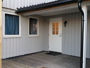 Gemütlicher Eingangsbereich eines nordnorwegischen Holzhauses mit weißer Tür und Fenster. Holzveranda vermittelt skandinavisches Flair, idealer Ausgangspunkt für Angelabenteuer in Nord-Norwegen. Perfekte Unterkunft für Naturliebhaber und Angler.
