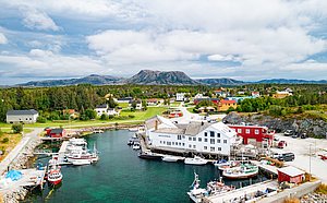 Luftaufnahme eines malerischen norwegischen Hafens in Hitra, umgeben von bunten Gebäuden und bewaldeten Hügeln. Perfekter Ausgangspunkt für abwechslungsreiche Angelabenteuer und unvergesslichen Angelurlaub im atemberaubenden Norwegen.