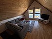 Gemütliches Wohnzimmer mit grauem Sofa in skandinavischem Holzhausstil. Große Fenster bieten Blick auf den Fjord in Hitra, Norwegen. Ideal für Angelurlauber und Naturliebhaber. Perfekte Balance aus Komfort und atemberaubender Landschaft.