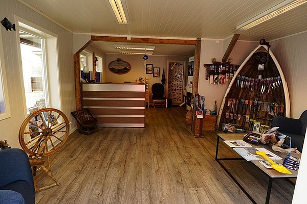 Gemütlicher Empfangsbereich in Nordland, Norwegen: Rustikale Atmosphäre mit Holzböden, Anglerbedarf, Infomaterial auf einem Tisch, Empfangstresen. Perfekt für Anglerreisen und Beratung. Ideal für Abenteuerlustige auf der Suche nach dem nächsten Fangabenteuer.