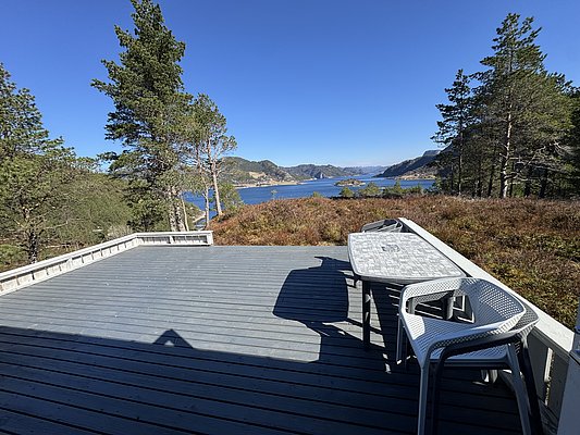 Große Terrasse mit Tisch und Stühlen vor malerischer Landschaft in Hitra, Norwegen. Blick auf bewaldete Hügel und klaren Fjord. Perfekt für entspannenden Angelurlaub und Naturliebhaber. Ideal für Erholung und Abenteuer in idyllischer Umgebung.
