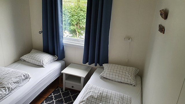 Gemütliches Schlafzimmer in Nord-Norwegen mit zwei Einzelbetten, blauen Vorhängen und Fensteraussicht ins Grüne. Ideal für Angelurlaub in ruhiger Umgebung. Skandinavisches Design mit minimalistischer Einrichtung und hellem Ambiente.