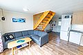 Gemütliches Wohnzimmer in Nord-Norwegen mit grauem Ecksofa, Holztisch und moderner Küche. Perfekte Unterkunft für Angelreisen im skandinavischen Stil. Helle, einladende Atmosphäre mit Holztreppe und mariner Wanddekoration.