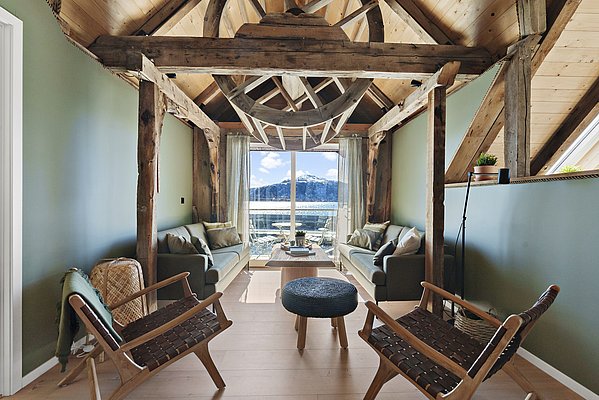Gemütliches Wohnzimmer in Südwest-Norwegen mit Holzelementen, modernen Möbeln und Panoramafenster. Blick auf verschneite Berge und Wasser. Ideal für entspannte Angelreisen und naturnahe Erholung.