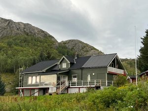Grünes Haus in Nordland, Norwegen, umgeben von bewaldeten Hügeln und felsigen Bergen. Ideal für Natur- und Angelreisen. Skandinavische Architektur harmoniert mit der beeindruckenden Landschaft. Perfekter Rückzugsort für Angler und Abenteuerlustige.