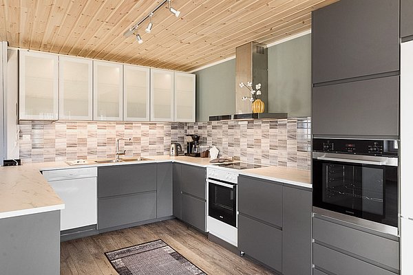 Moderne Küche in Nordland, Norwegen, mit stilvollem Design: graue Schränke, helle Holzdecken, gestaltete Fliesenwände und hochwertige Geräte. Perfekt für Anglerurlaube oder entspannte Kochabende nach einem erfolgreichen Angelausflug.