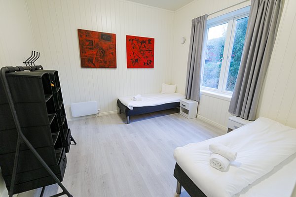 Helles, gemütliches Schlafzimmer in Nordland, Norwegen mit zwei Einzelbetten, modernen Kunstwerken an weißen Wänden und Blick auf die Natur. Ideal für Angelreisende, die Komfort und Entspannung suchen.