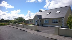 Gemütliches irisches Bungalowhaus in Boyle, Irland. Ein gepflegter Garten umgibt das helle Gebäude. Der blaue Himmel und weiße Wolken sorgen für eine freundliche, einladende Atmosphäre. Perfekt für einen entspannenden Aufenthalt im Grünen.