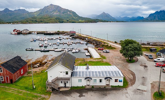 Kleiner Hafen in Nordland, Norwegen, umgeben von Bergen und Fjorden. Boote liegen am Steg, traditionelle Holzhäuser und grünes Terrain bieten eine malerische Kulisse für Angelabenteuer. Ideal für einen erholsamen Angelurlaub.