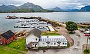 Kleiner Hafen in Nordland, Norwegen, umgeben von Bergen und Fjorden. Boote liegen am Steg, traditionelle Holzhäuser und grünes Terrain bieten eine malerische Kulisse für Angelabenteuer. Ideal für einen erholsamen Angelurlaub.