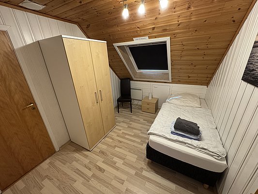 Ein gemütliches, schlichtes Schlafzimmer in Hitra, Norwegen, mit Einzelbett, Kleiderschrank und Dachfenster. Ideal für entspannte Angelurlaube und entspannende Aufenthalte in der Natur.