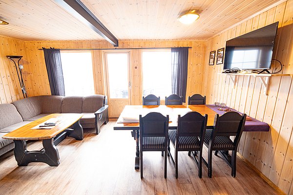 Gemütliches Ferienhaus in Nordland, Norwegen: Helle Holzwände, große Fenster, bequeme Sofas, Esstisch und Fernseher, ideal für Angler. Perfekte Unterkunft für Angelreisen in der malerischen Natur Skandinaviens.